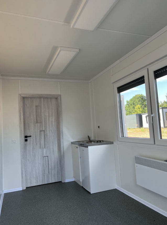 Raumecke mit LED-Deckenleuchten, Zimmertür in Holzoptik und der weißen Küchenzeile am Fenster