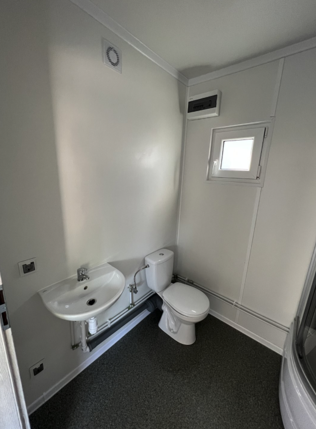 Sanitärbereich mit Wandwaschbecken, Stand-WC, Klappfenster und Lüftungsgitter in der Decke
