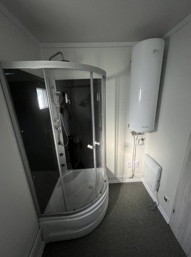 Duschecke im Bad, rechts der wandhängende Boiler mit Anschlussleitungen und ein kleines Heizgerät