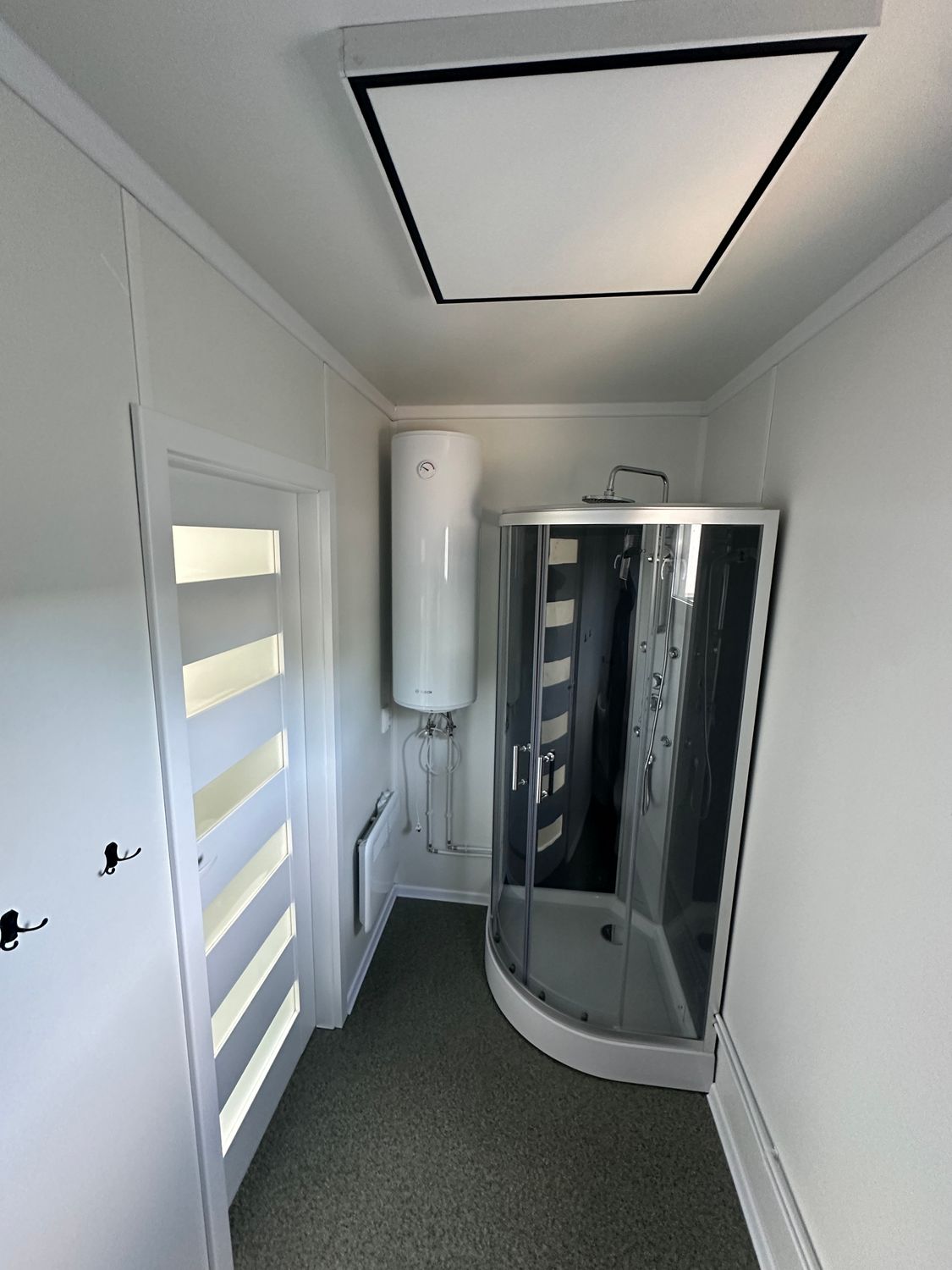 Duschraum mit Eckduschkabine, Warmwasserboiler an der Wand und Zimmertür mit Streifenglas