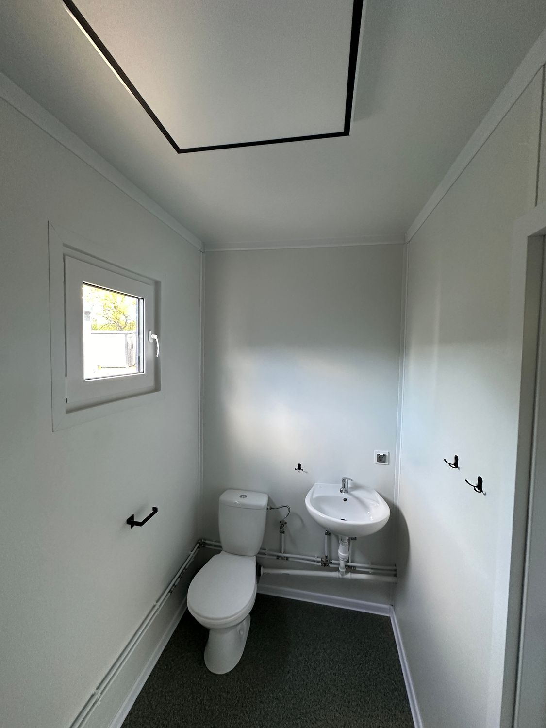Toilettenraum mit Stand-WC, Eckwaschbecken, Klappfenster und Handtuchhaken an der Wand