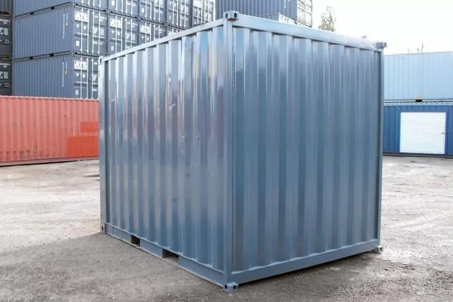 Von der gegenüberliegenden Ecke zeigt sich der graue Container mit Wellblechwänden und Stapelecken