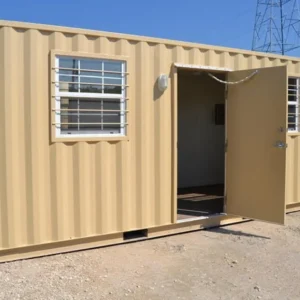 Geöffnete Tür und vergittertes Fenster am sandfarbenen 20-Fuß-Bürocontainer, aufgestellt auf Kies