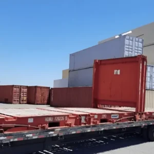 Rotbraune gebrauchte 20-Fuß-Flatrack-Container mit hochgeklappten Stirnwänden auf einem Tieflader