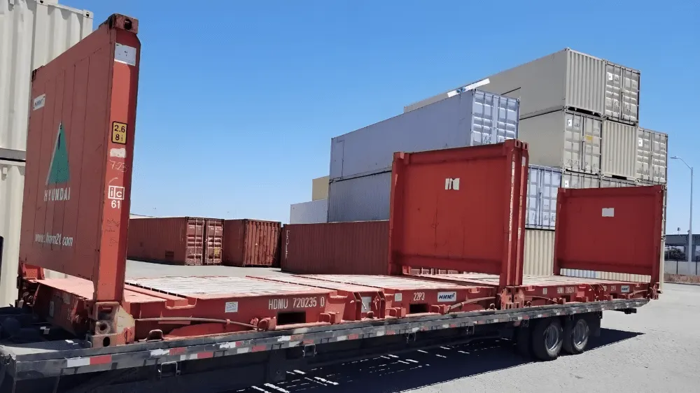 Rotbraune gebrauchte 20-Fuß-Flatrack-Container mit hochgeklappten Stirnwänden auf einem Tieflader