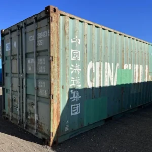 Schrägansicht des petrolfarbenen 20-Fuß-Lagercontainers mit Türseite, Reederei-Aufschrift und Rostspuren