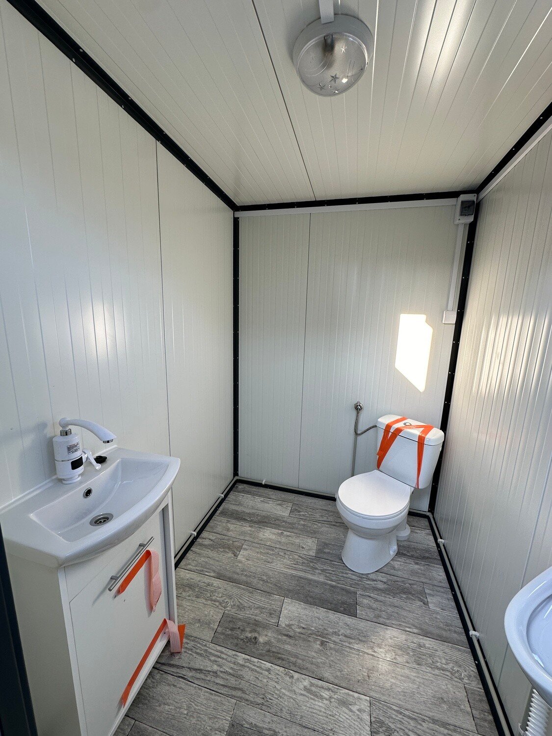 Blick über Waschtisch und Toilette in der hell verkleideten Sanitärkabine des Doppel-WC Containers