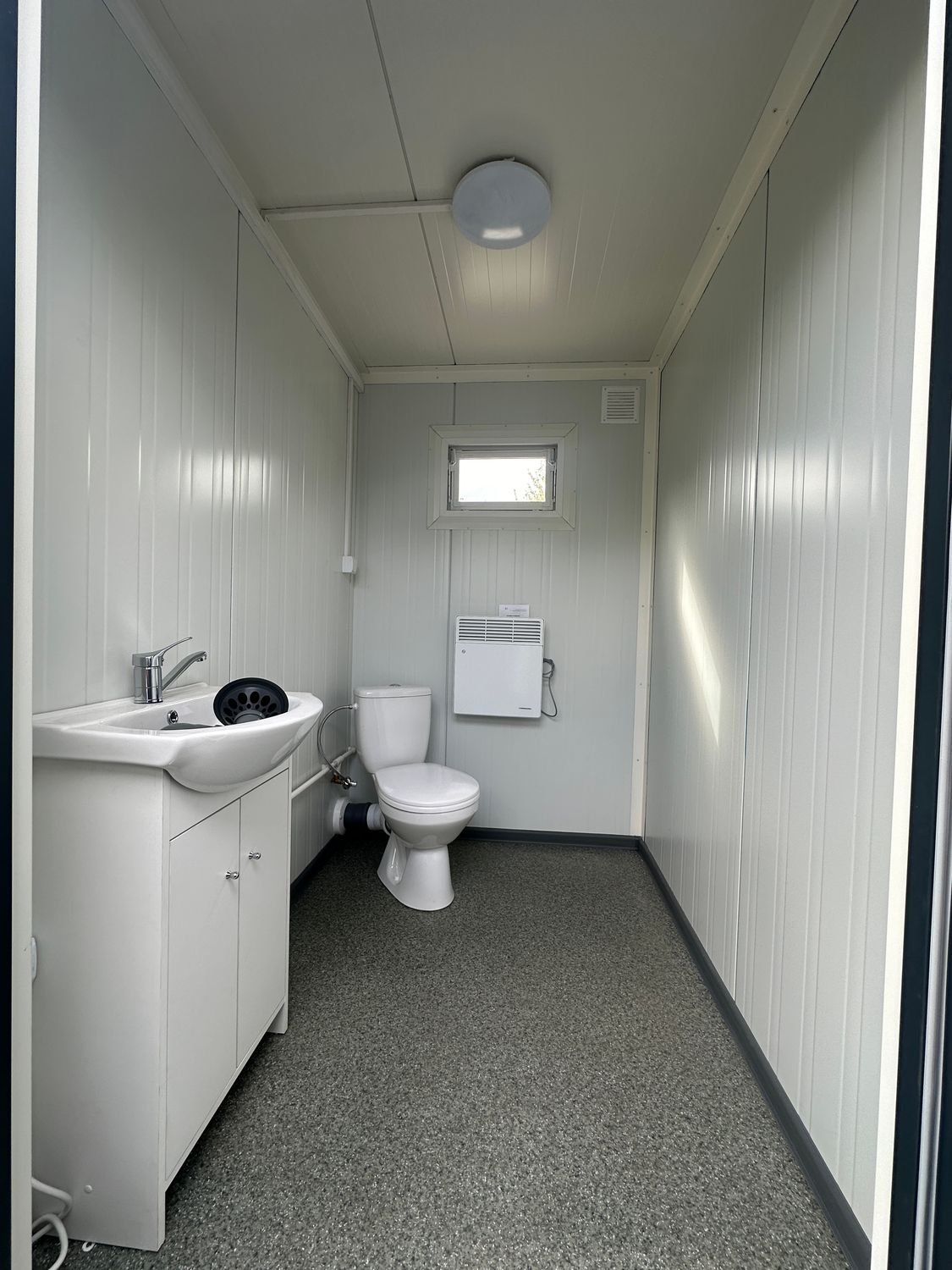 Zweite Kabine des Doppel-WC Containers mit Waschbecken, Toilette, Heizkörper und Fenster über dem WC