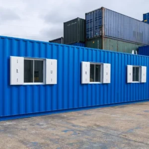 Blauer 40-Fuß-Bürocontainer mit drei weiß gerahmten Fenstern und Seitentür auf einem Containerstellplatz