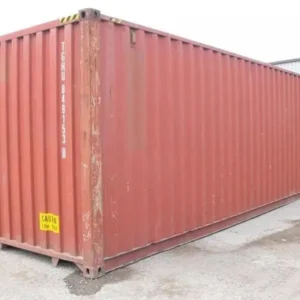 Rotbrauner 40-Fuß-High-Cube-Container in Schrägansicht auf befestigtem Hof, Halle im Hintergrund