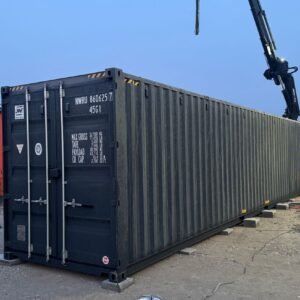 Seitenansicht des 40 Fuß Lagercontainers in Dunkelgrau, abgesetzt auf Betonplatten neben einem Ladekran