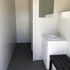 Innenansicht des 40-Fuß-Sozial- und Prüfcontainers mit Waschbecken, Spiegel, Sitzbank und grauem Boden