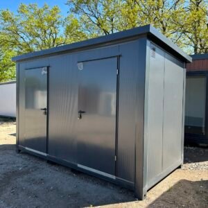 Komplett anthrazitfarbener Doppel-WC- und Duschcontainer mit zwei Türen und Lüftungsgitter auf Kiesfläche
