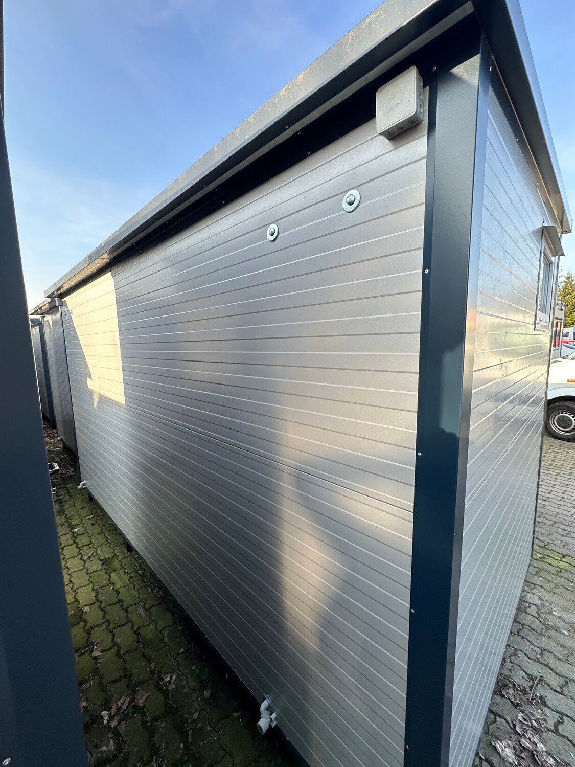 Fensterlose Längsseite des Duschcontainers mit Abzweigdose unter der Dachkante und Abflussrohr am Boden