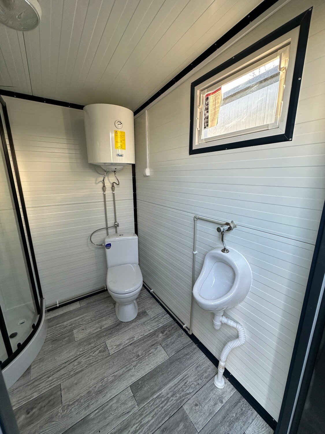 Sanitärraum mit Boiler über dem WC, Urinal an der Trennwand und Kippfenster darüber