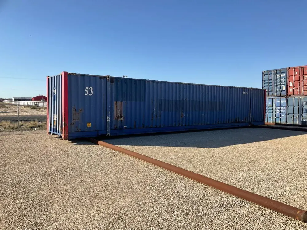 Langseite des blau lackierten 53-Fuß-Containers auf Kies, rote Stirnkante, gestapelte Container dahinter