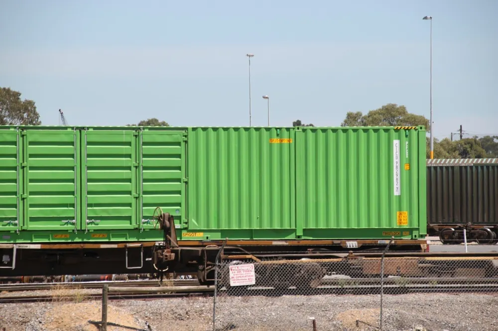 Grüner Container auf einem Eisenbahnwaggon, daneben eine Einheit mit geschlossenen Seitentüren