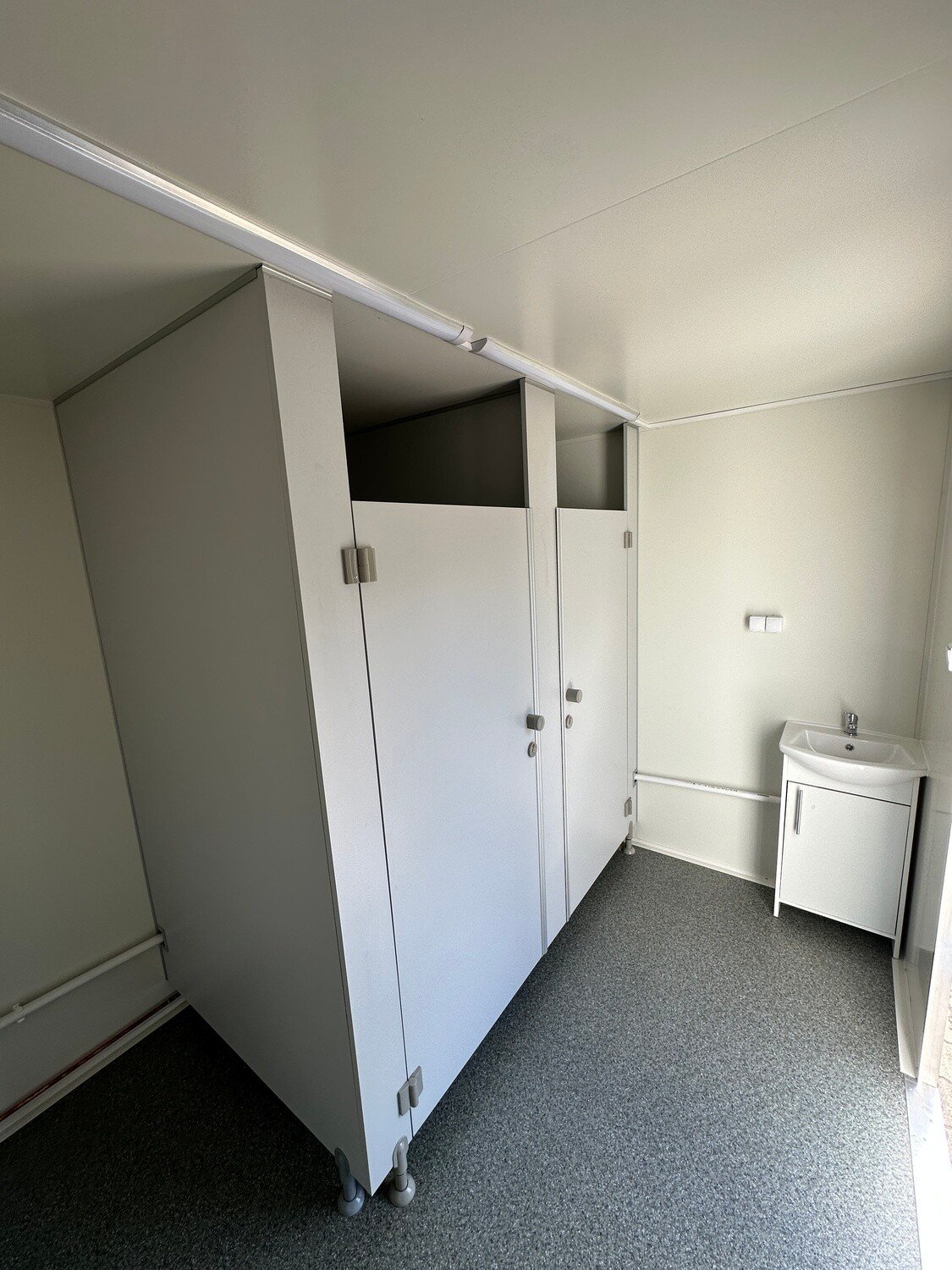 Sanitärraum mit zwei Toilettenkabinen, Waschtisch mit Unterschrank und Lichtleiste an der Decke
