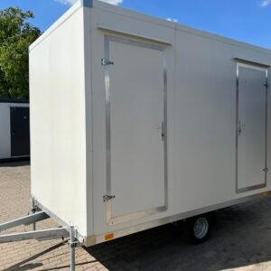 Außenansicht des WC-Anhängers mit zwei Eingangstüren, Deichsel und Einzelachse auf gepflastertem Platz
