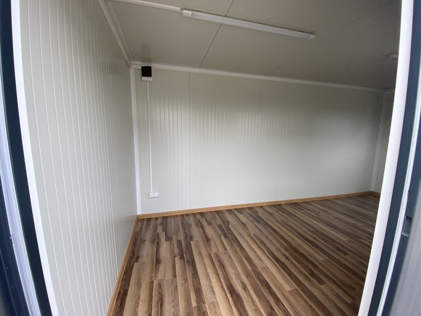 Durch die offene Tür fotografierter Innenraum mit Deckenleuchte, Steckdose und Holzdekorboden