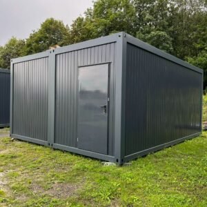 Außenansicht des Doppelcontainers über Eck, anthrazitfarbene Trapezwände mit einer Tür, auf Wiese