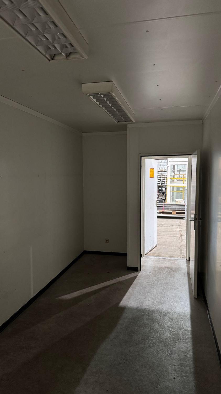 Raumtiefe mit Rasterleuchten und geöffneter Außentür, Blick hinaus auf den Lagerplatz