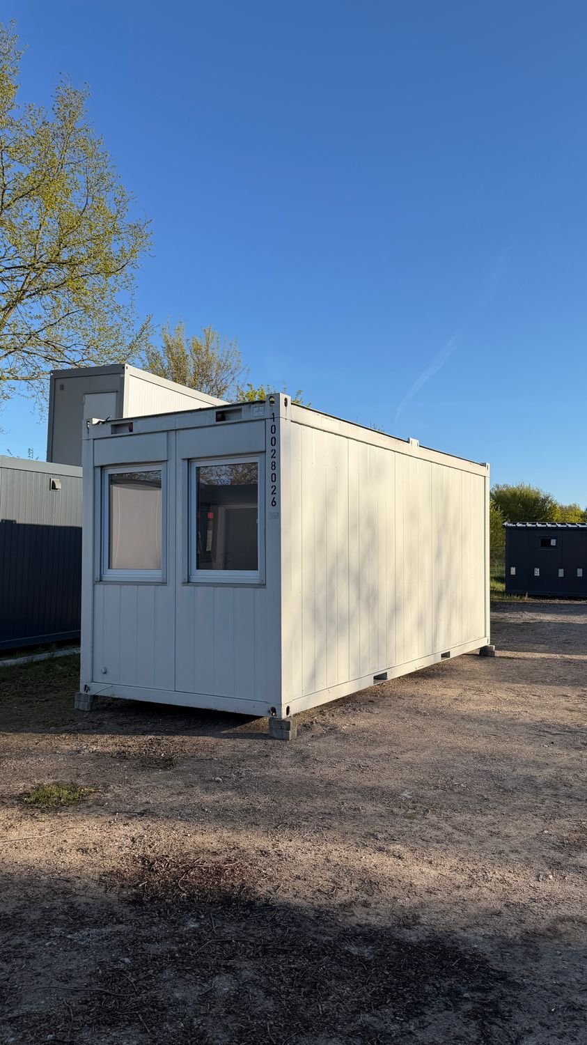 Auf Stapelklötzen stehender Bürocontainer mit zwei Fenstern, Außenaufnahme bei Sonnenschein
