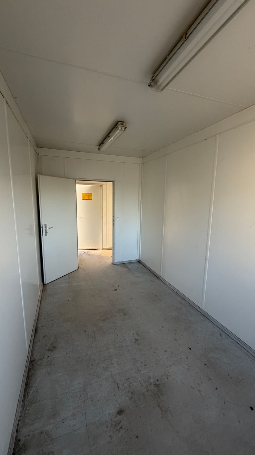 Zweiter Raum mit geöffneter Verbindungstür, Leuchtstofflampen und glatten Wandpaneelen