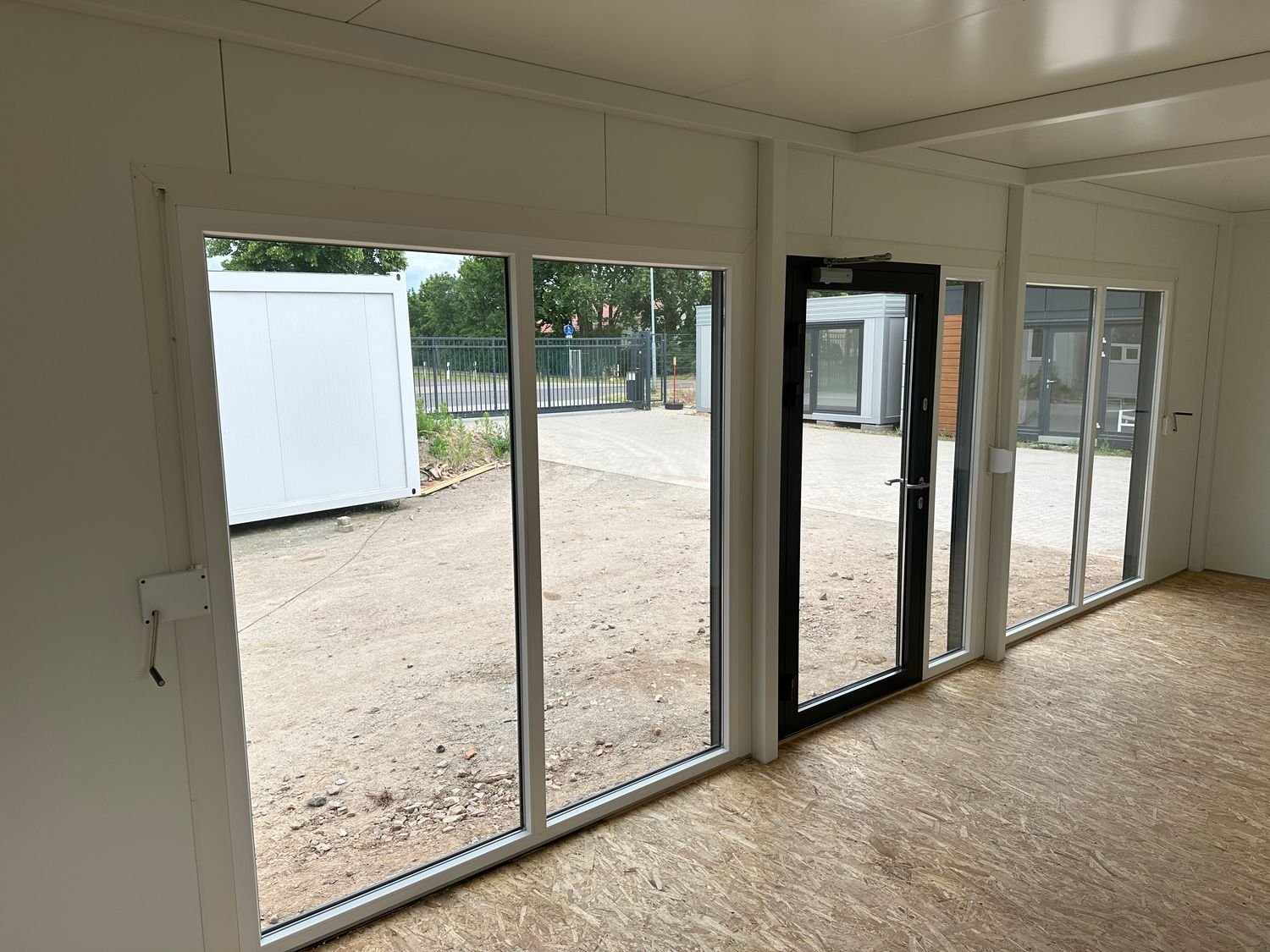 Innenansicht mit raumhoher Fensterfront, dunkler Glastür und OSB-Boden im Imbisscontainer
