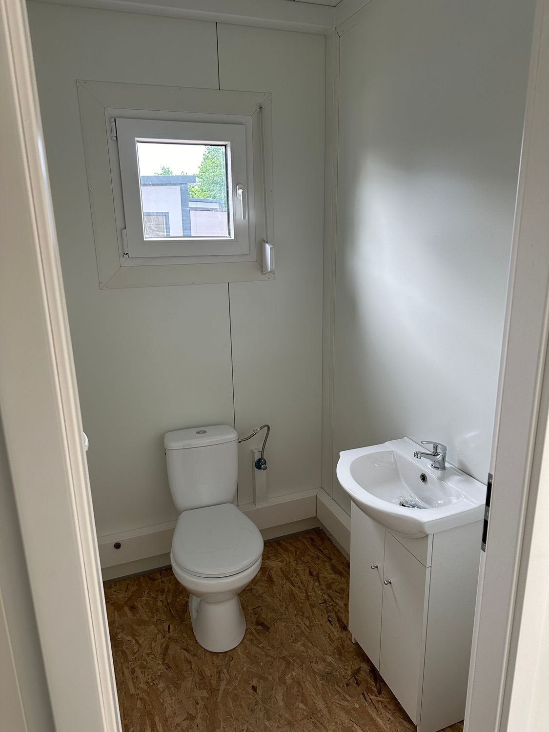 Sanitärraum des Imbisscontainers mit WC, Waschbecken auf Unterschrank und geöffnetem Kippfenster