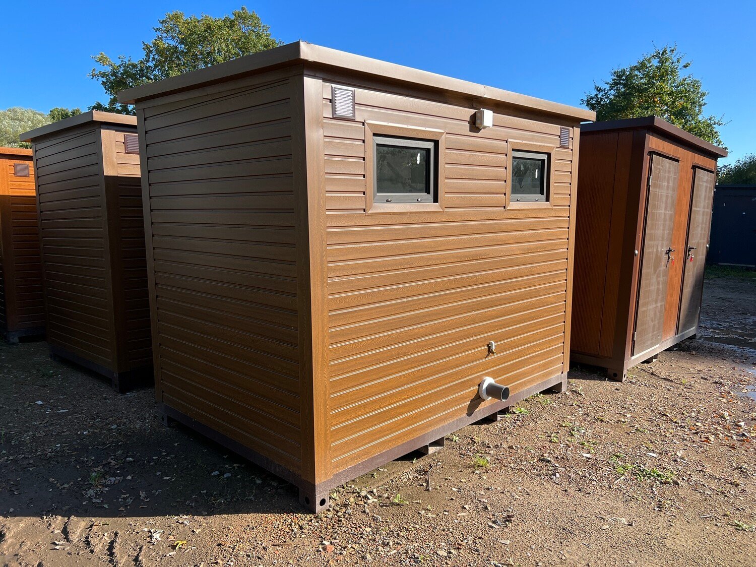 Rückseite mit zwei kleinen Fenstern, Lüftungsgitter und Abwasserstutzen am Premium Doppel-WC Container