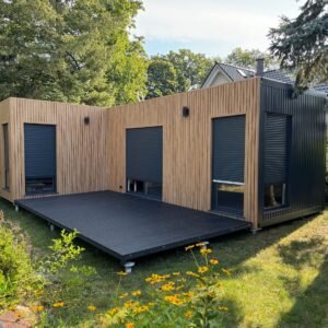 Außenansicht des Premium Tiny House in L-Form mit Holzfassade, anthrazitfarbenen Rollläden und Terrasse
