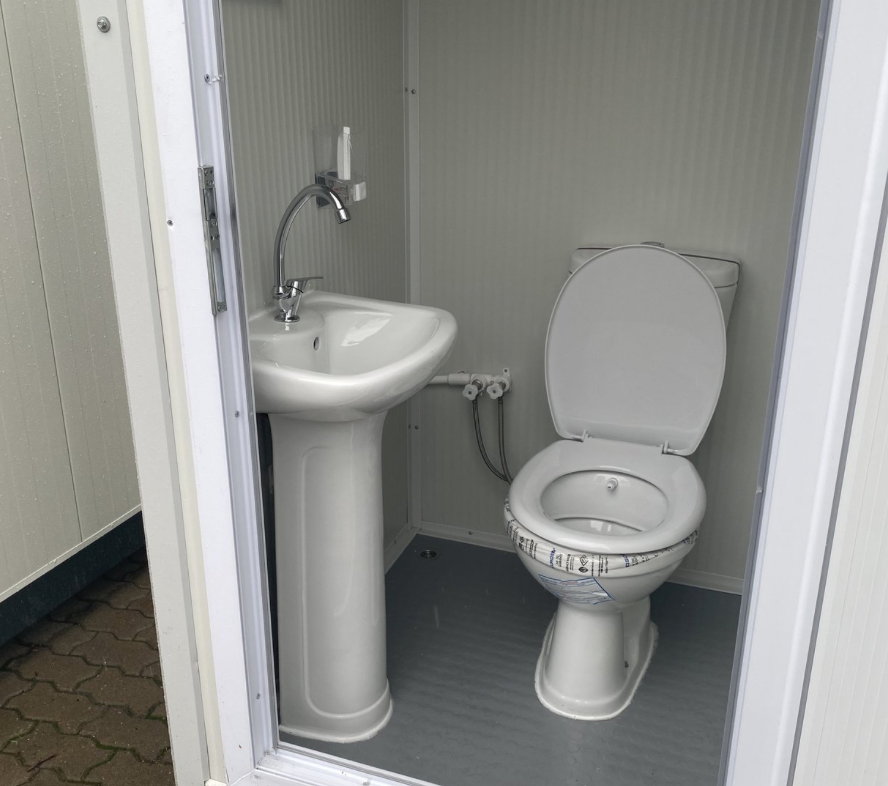 Innenansicht mit Standwaschbecken, Armatur, WC und grauem Bodenbelag des Sanitärcontainers