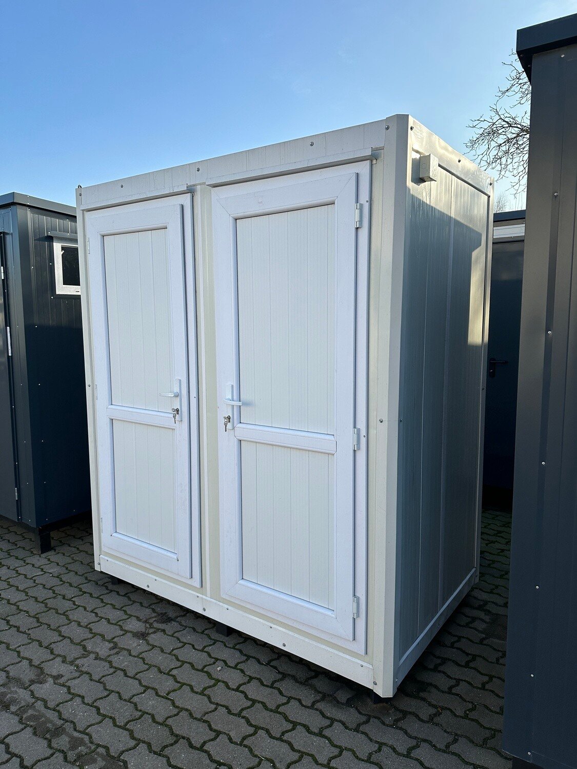 Außenansicht des Sanitärcontainers 1,30 x 2,05 m mit zwei weißen Türen auf Pflasterfläche