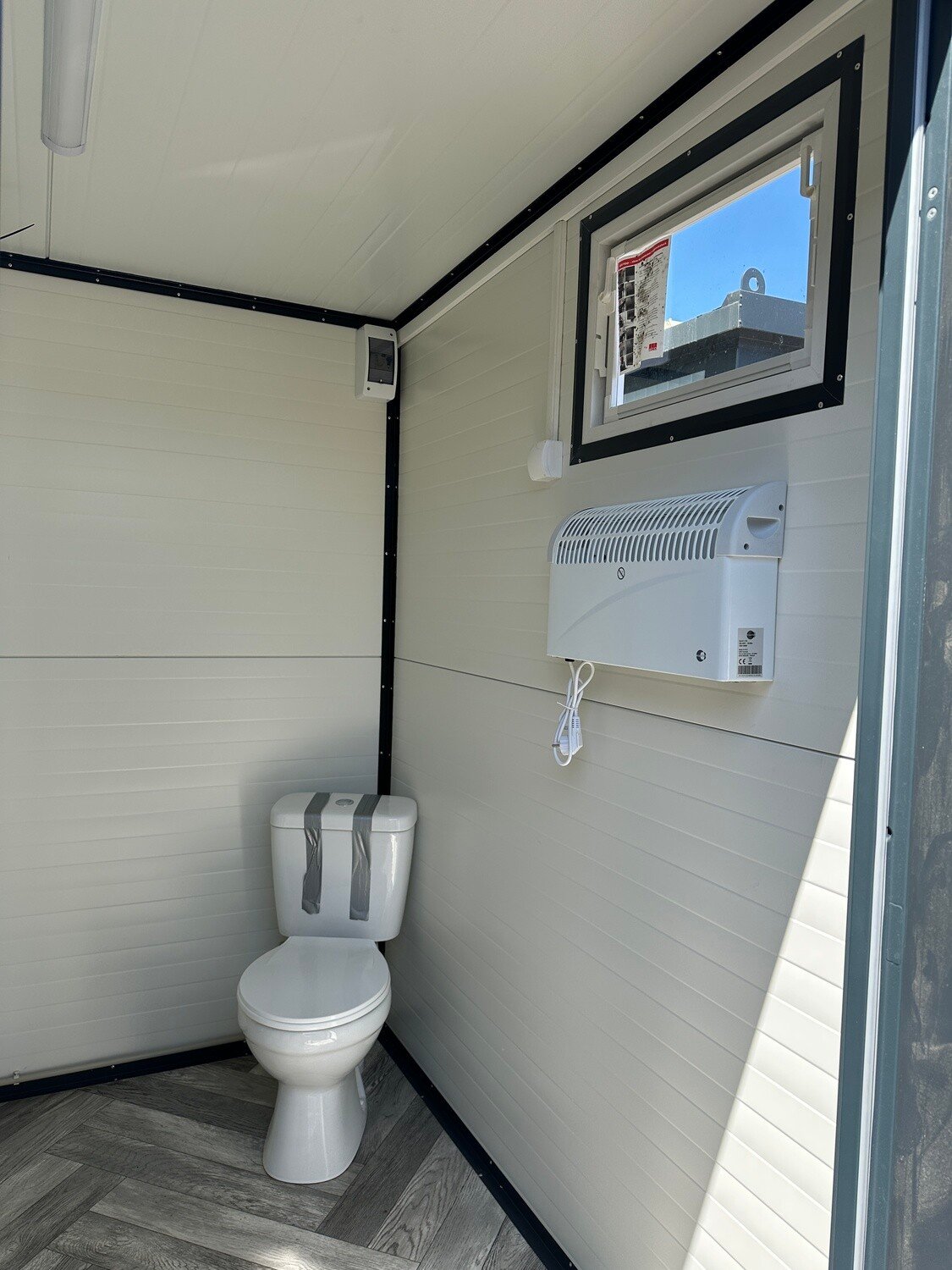 Blick in die WC-Ecke mit Wandkonvektor, Fenster und Fischgrätboden, Sanitärcontainer 2,00 x 2,00 m