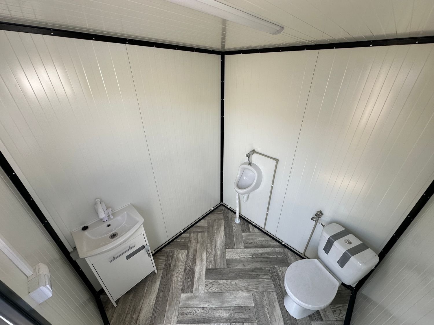 Innenansicht von oben mit Waschtisch, Wandurinal und WC auf Fischgrätboden im Sanitärcontainer
