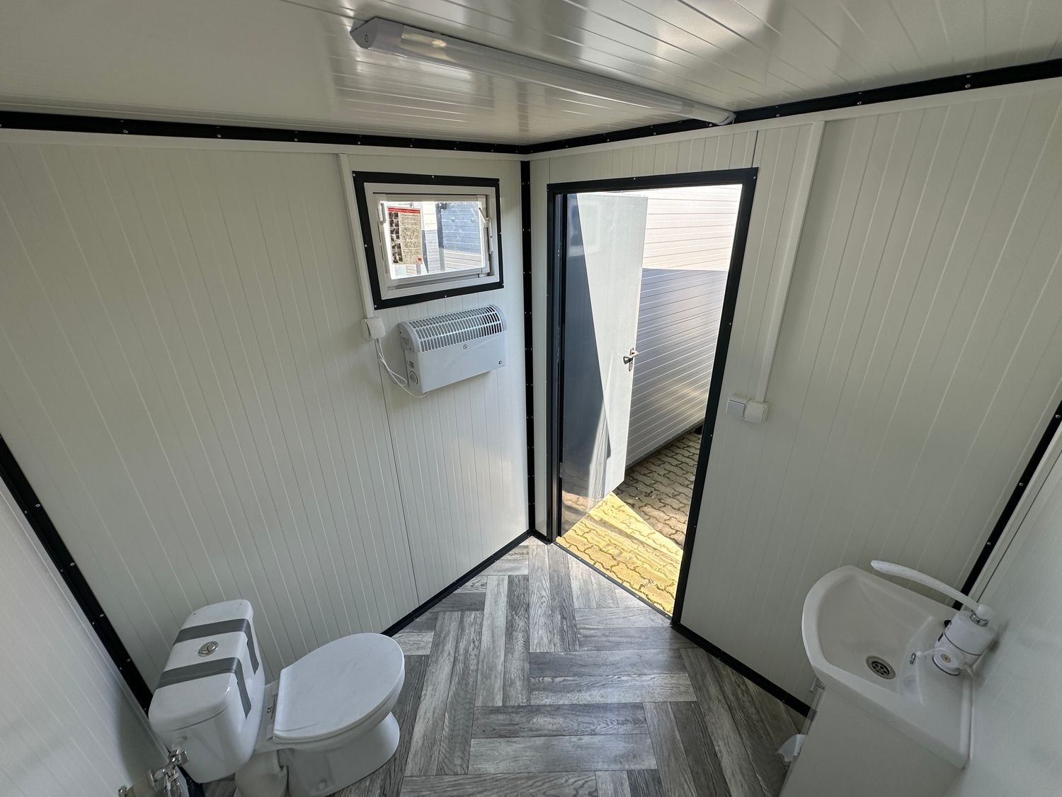 Von innen zur offenen Tür fotografiert: WC, Handwaschbecken, Fenster und Heizgerät an der Wand