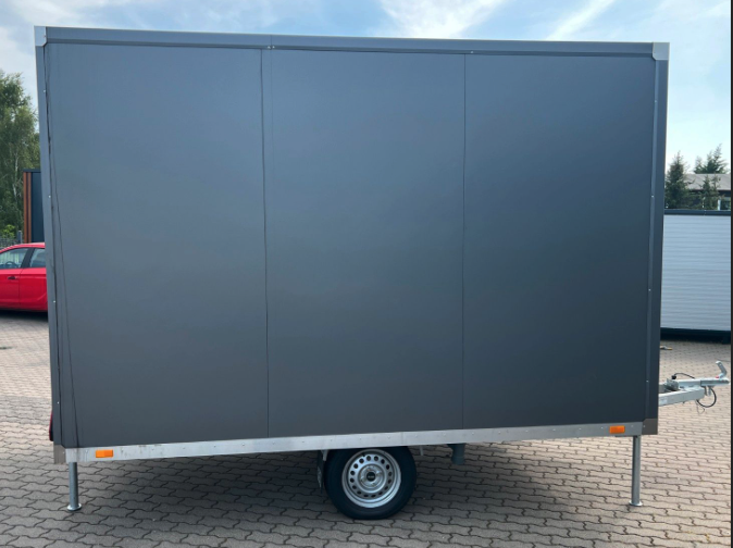 Fensterlose Längsseite des WC-Anhängers, darunter Rad, Stützfüße und orangefarbener Reflektor
