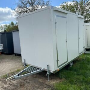 Weißer WC-Anhänger mit Toilette und Dusche schräg von vorn, zwei Türen und Deichsel auf Wiese