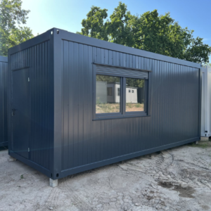 Außenansicht des Wohncontainers 6,00 x 2,44 in Anthrazit mit Eingangstür und breitem Fenster auf Sandfläche